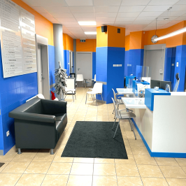 Na zdjęciu widoczna jest poczekalnia dla pacjentów. Ściany są niebiesko-pomarańczowe i kontrastują do białych krzeseł, sufitu i jasnej podłogi.